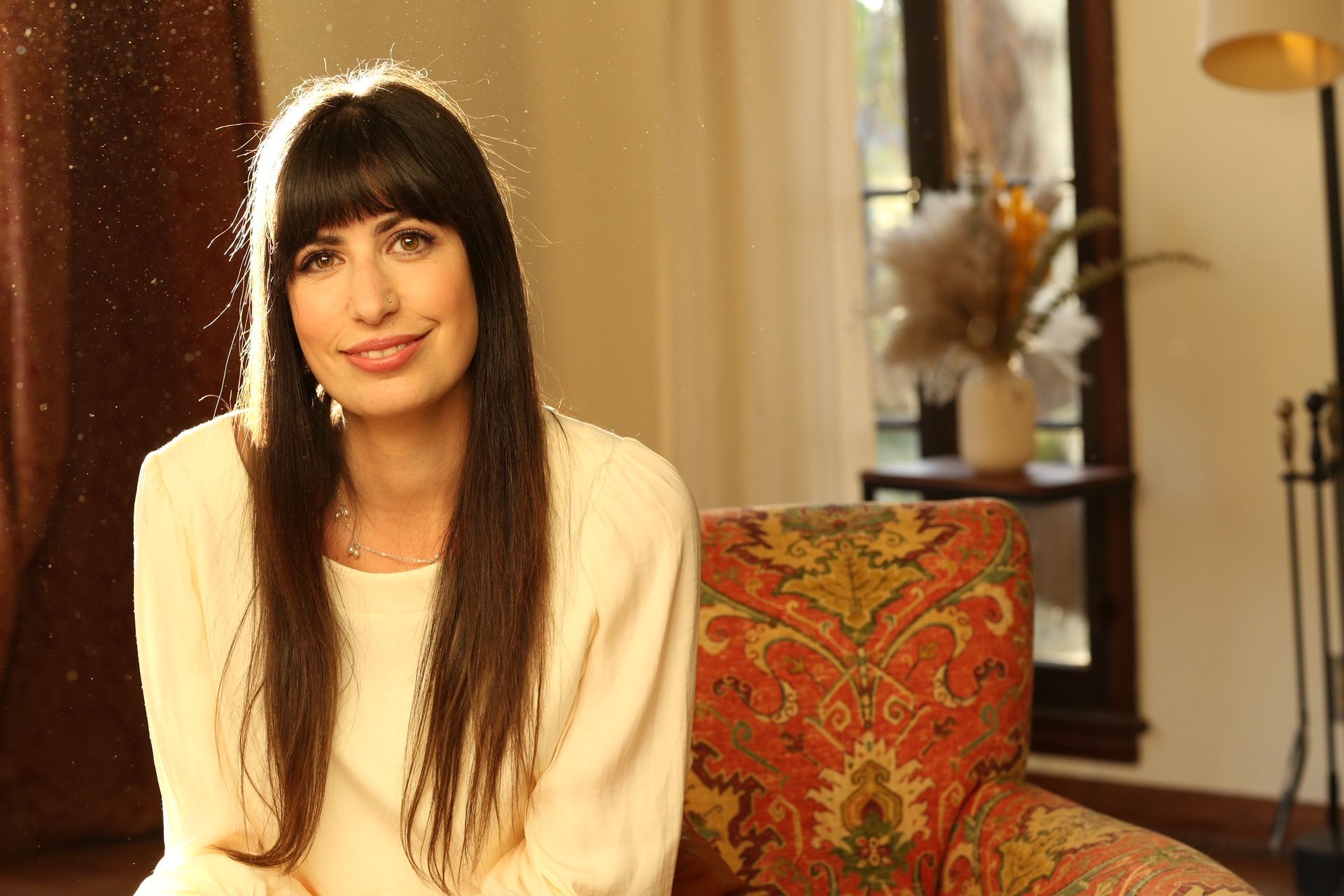A pregnant woman in a red dress is sitting on the grass.