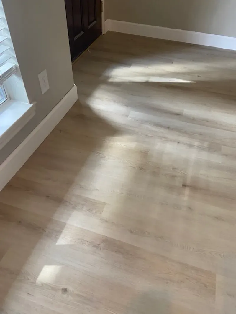 Sunlit hardwood floor in an empty room with white baseboards and beige walls