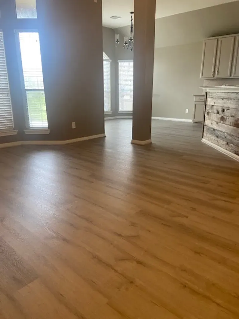 Empty living room with wood floors, tall windows, and a beige accent wall
