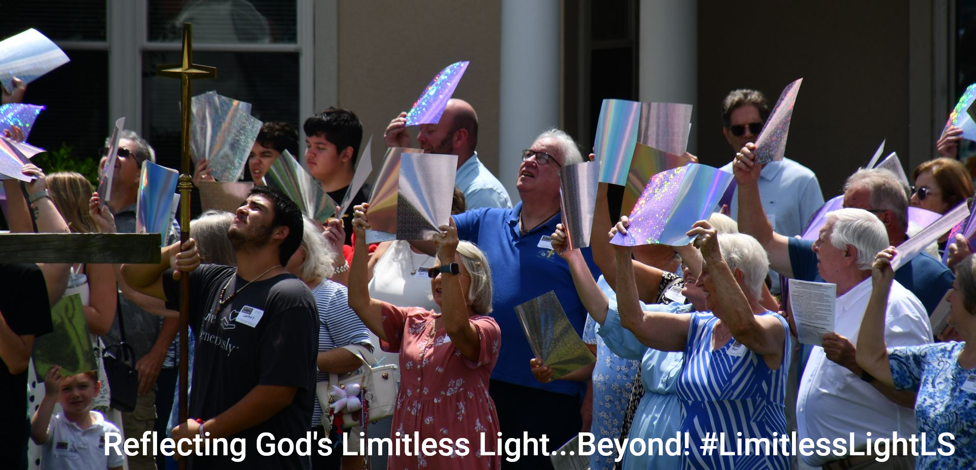 People holding up colorful papers, looking upward in a sunny outdoor setting near a building.