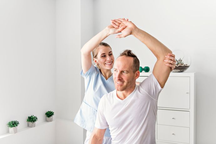 Two people doing a stretching exercise in a bright therapy room
