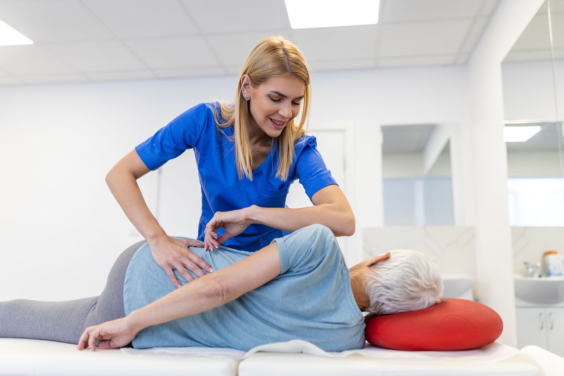 Physical therapist in blue helping a patient stretch on a treatment table in a bright clinic