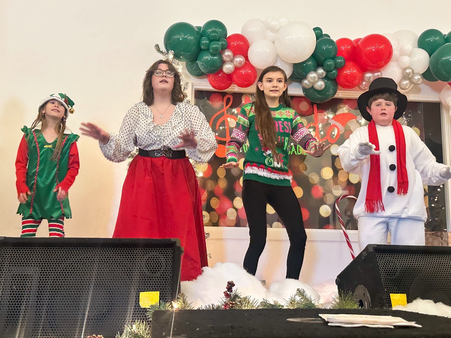 A group of children dressed in christmas costumes are dancing on a stage.