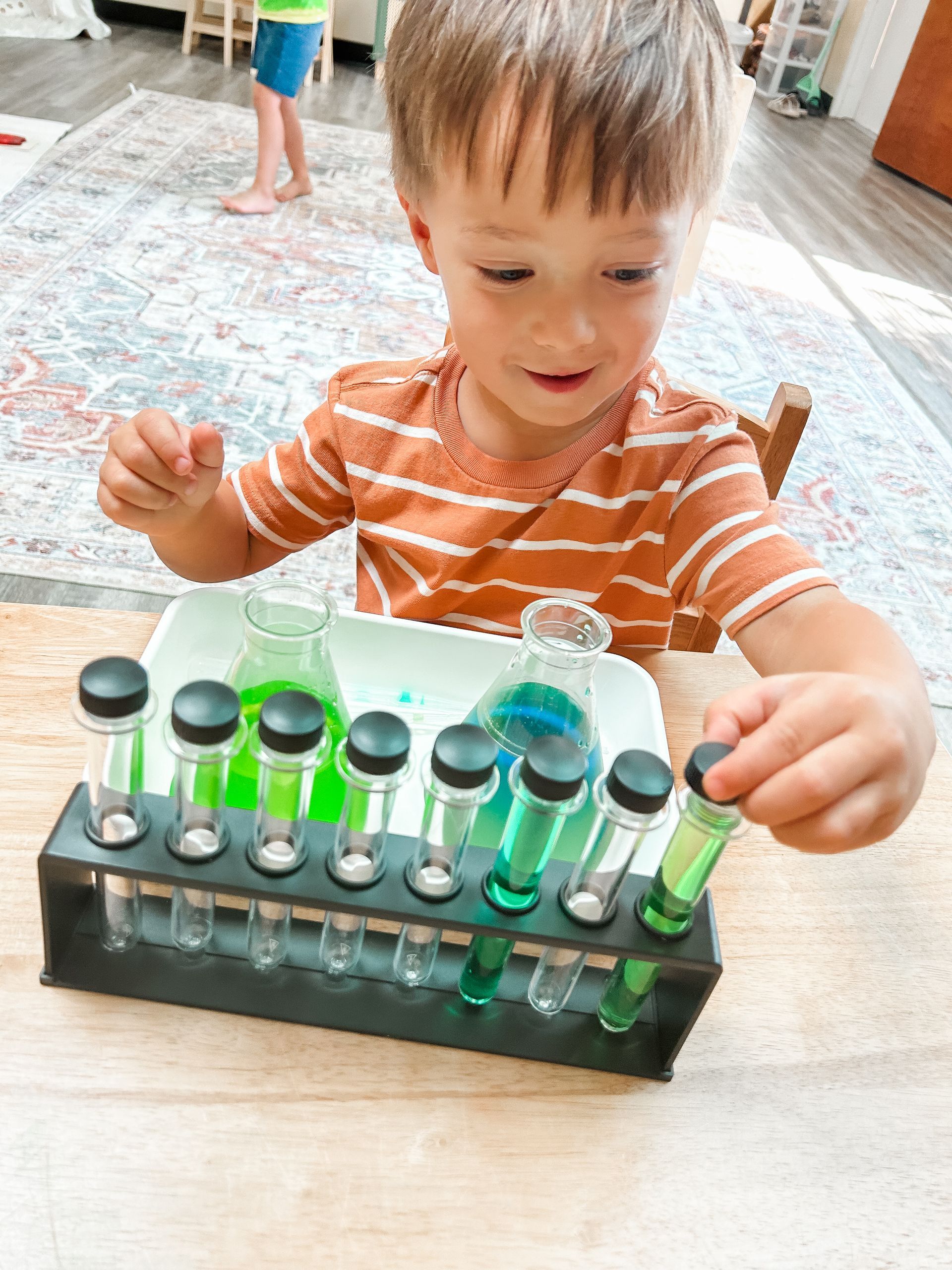 A young boy is sitting at a table playing with test tubes and a pipette.