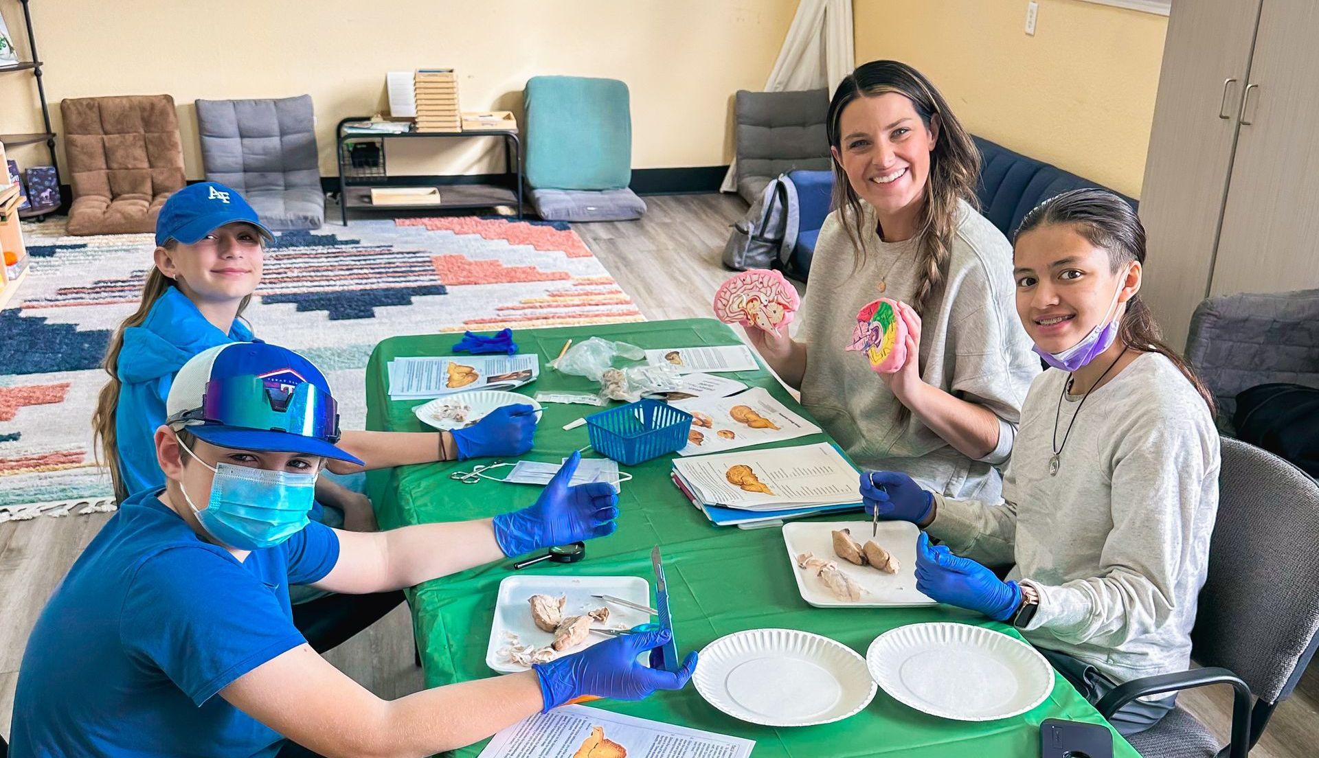 Three young girls wearing blue gloves are sitting at a table.