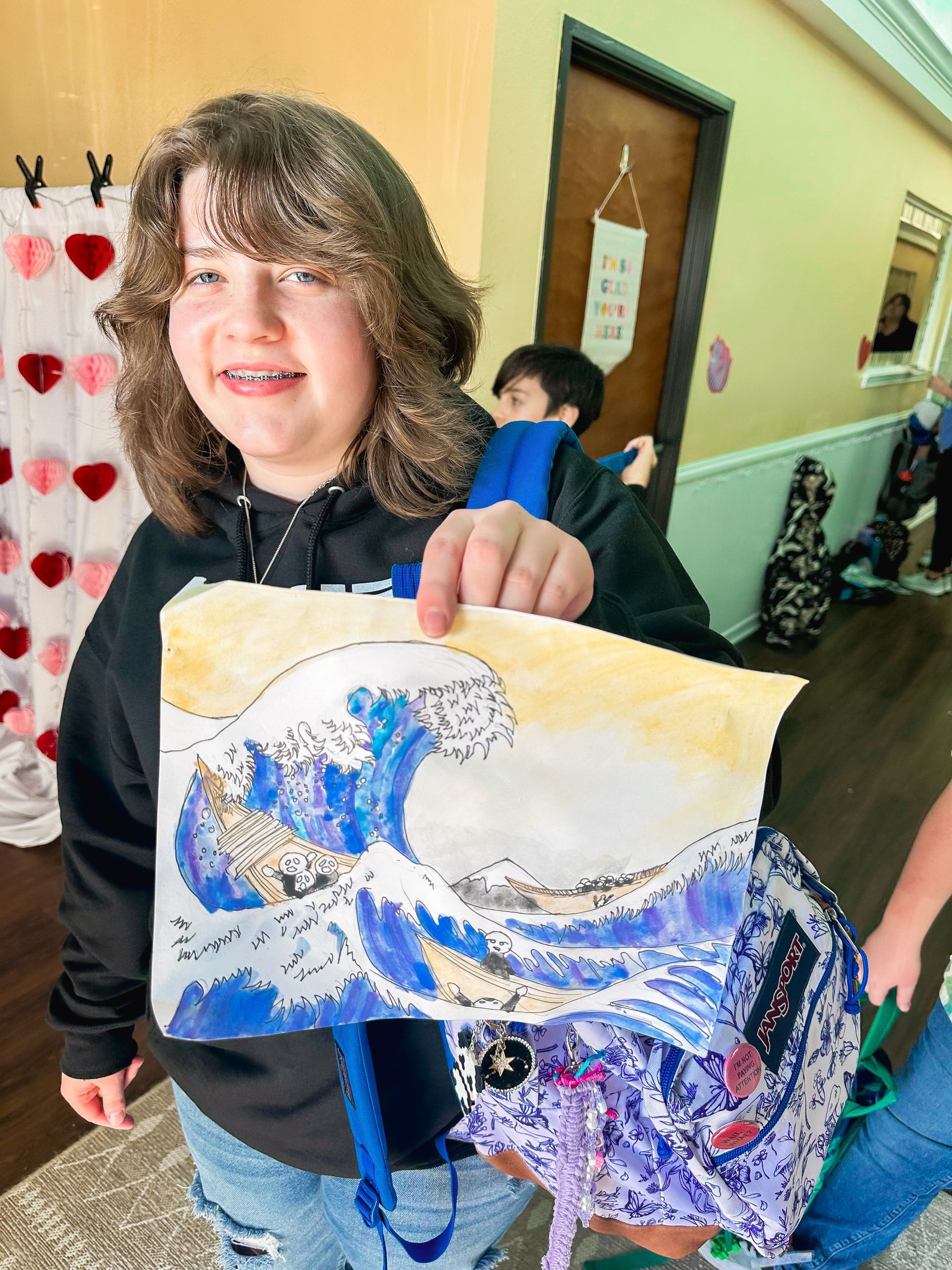 A young girl is holding a piece of paper with a picture of a wave on it.
