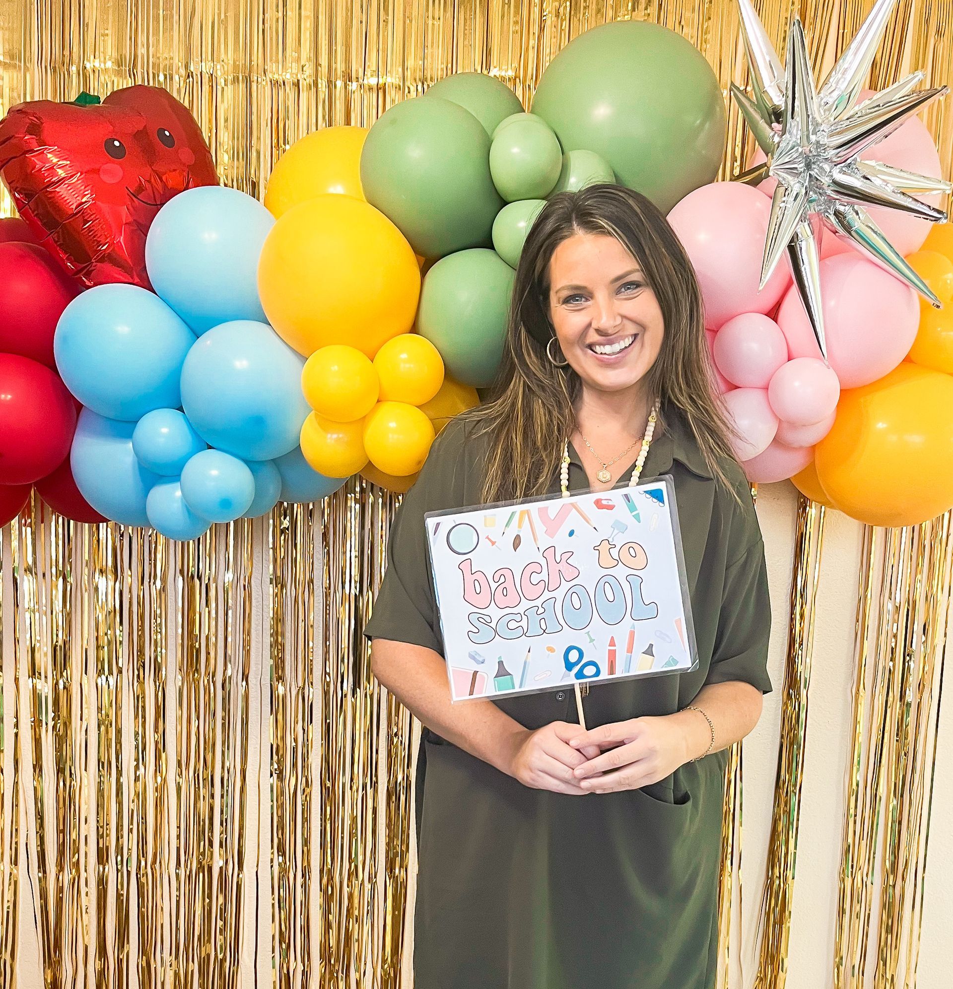 A woman is holding a sign that says `` back to school '' in front of balloons.