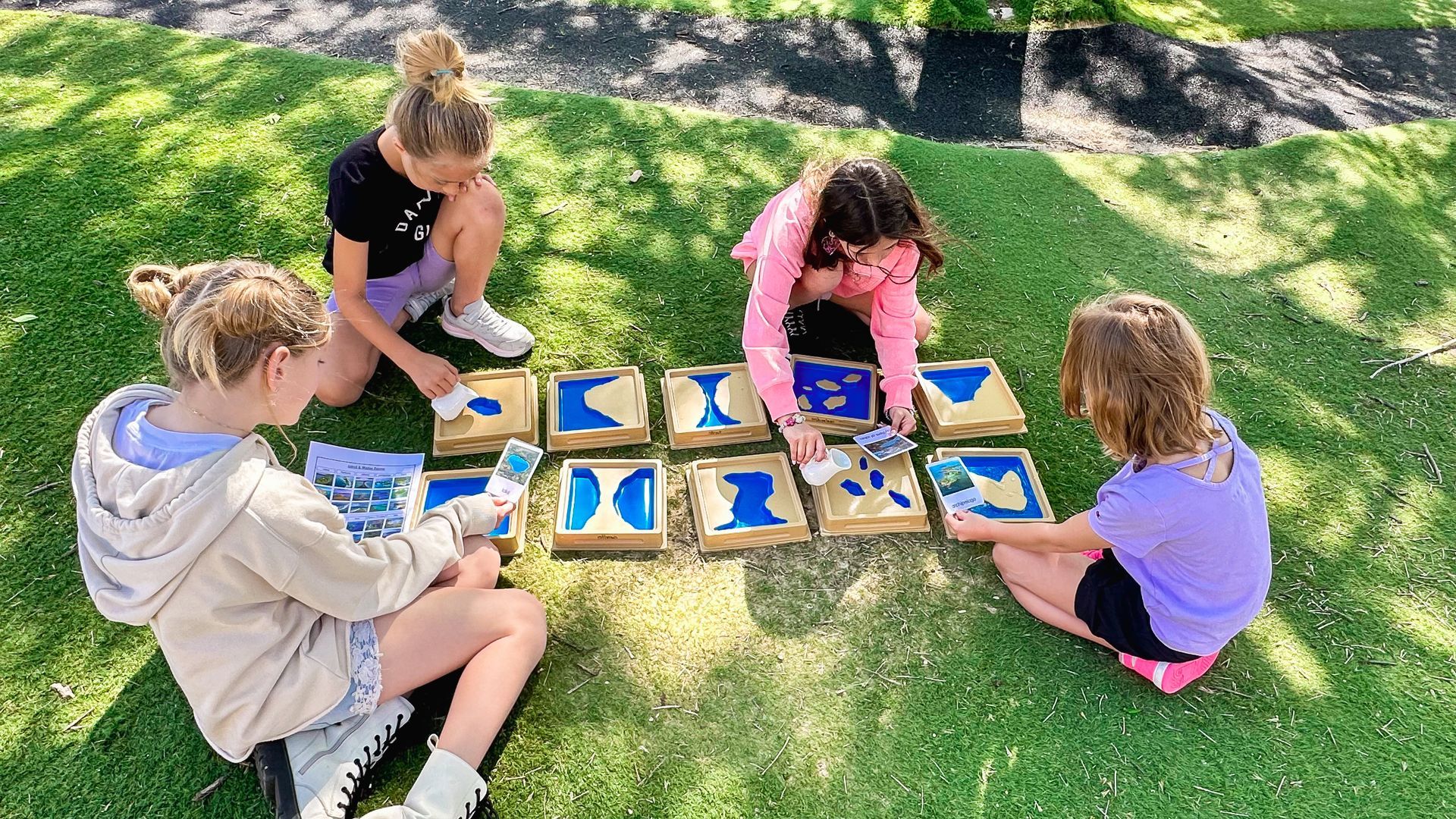A group of young girls are sitting on the grass playing a game.