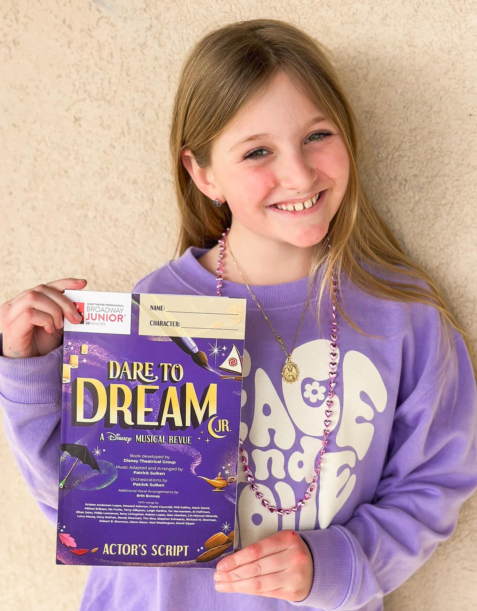 A girl wearing a purple sweatshirt and a white beanie is holding a donut.