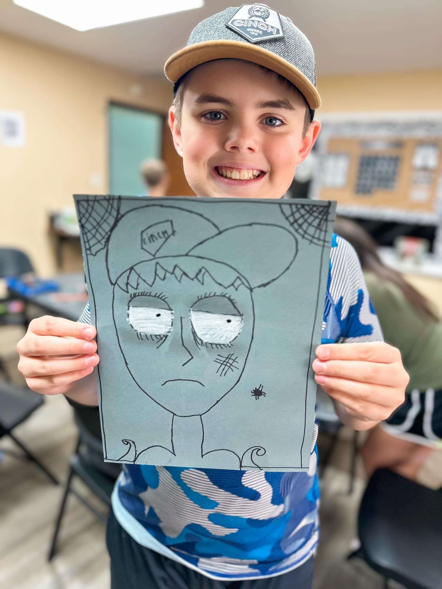 A young boy is holding a drawing of himself in a baseball cap.