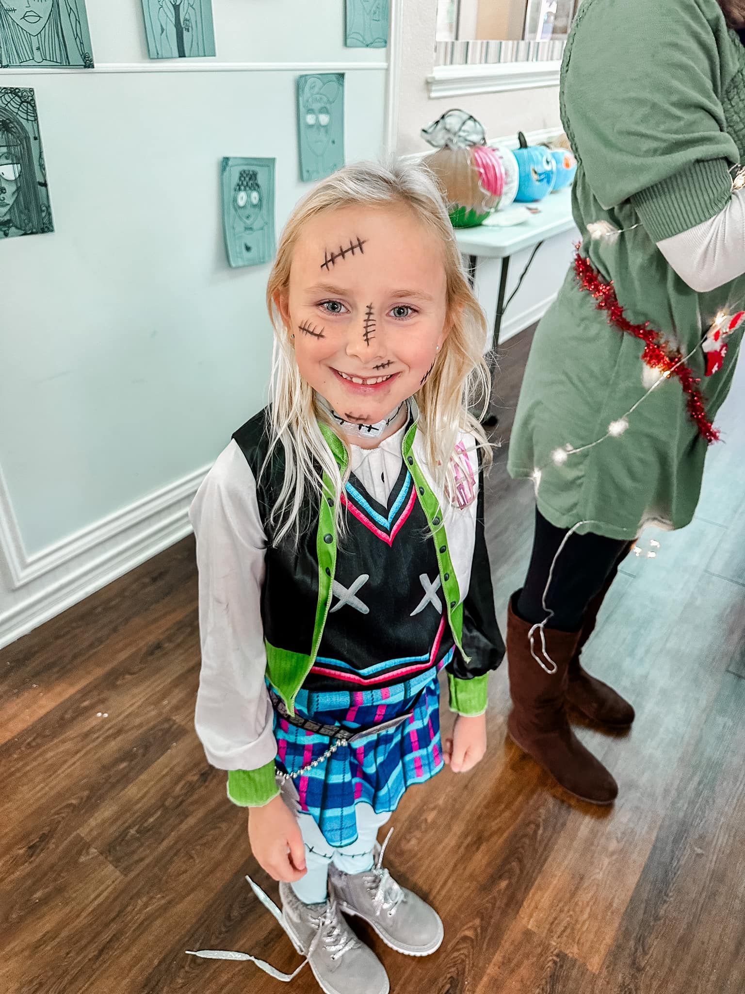 A little girl in a frankenstein costume is standing on a wooden floor.