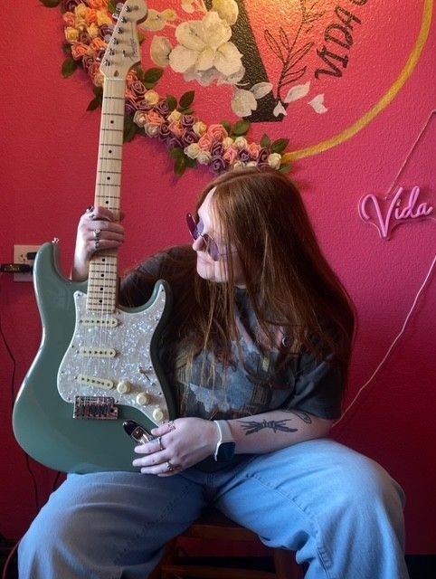 A woman is holding a guitar in front of a pink wall that says vida