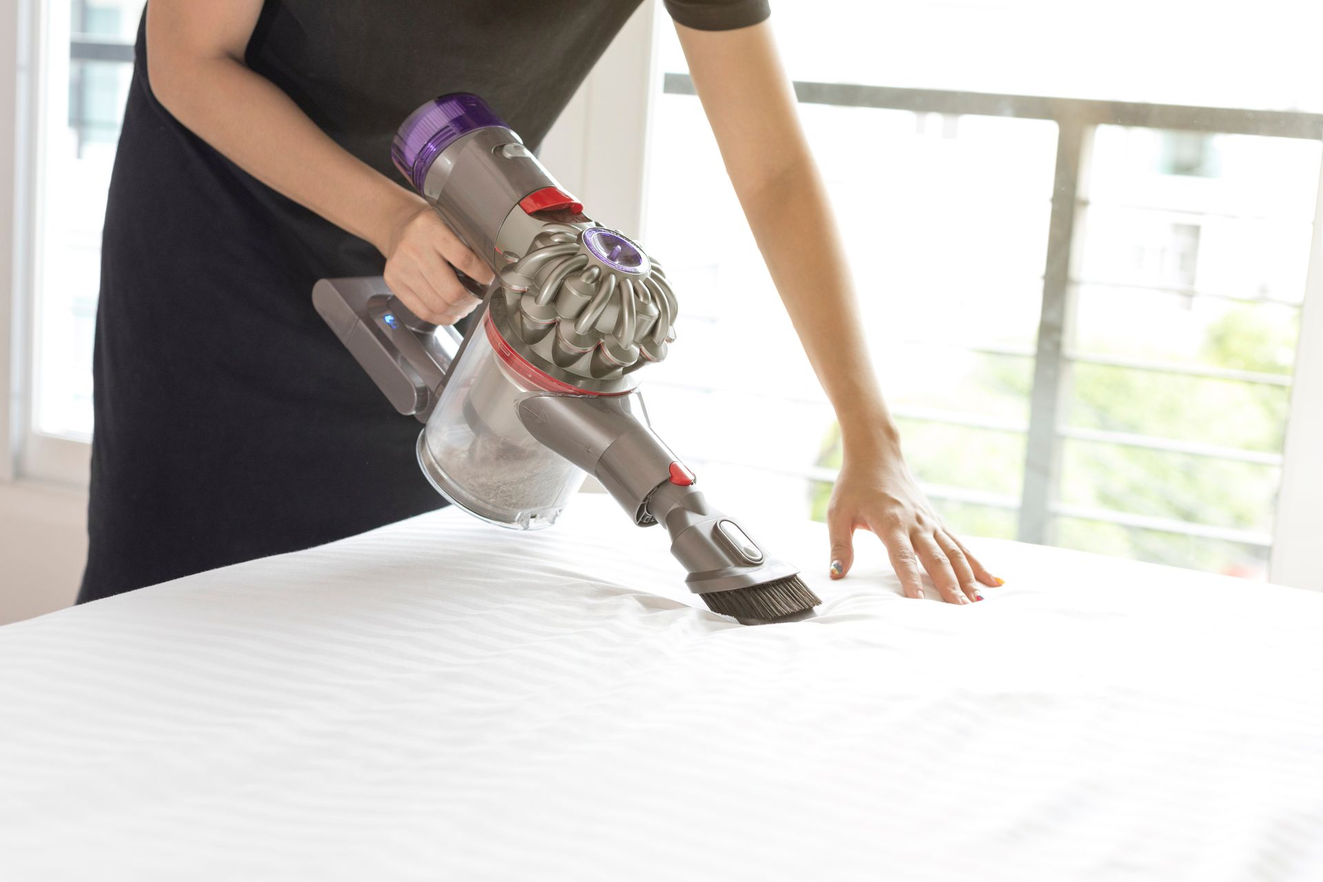 A woman is cleaning a bed with a vacuum cleaner.