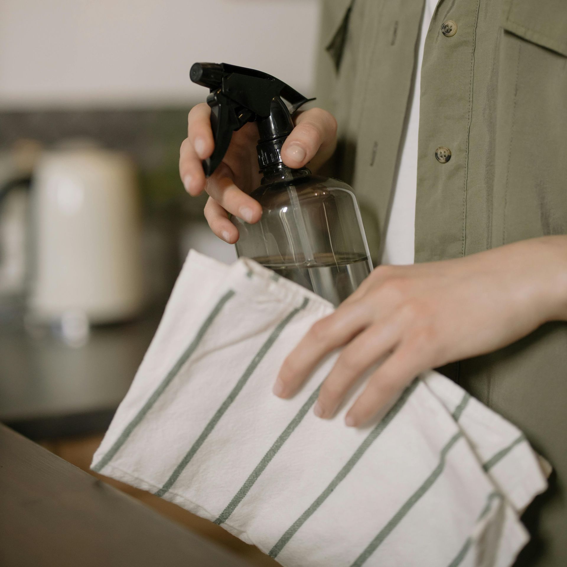 A person is holding a spray bottle and a striped towel.