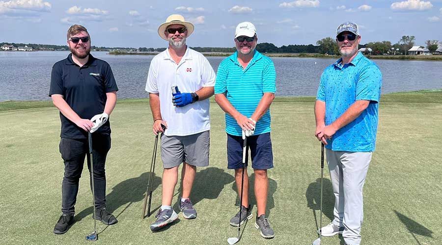 Four men standing on a golf course, holding clubs, smiling. L