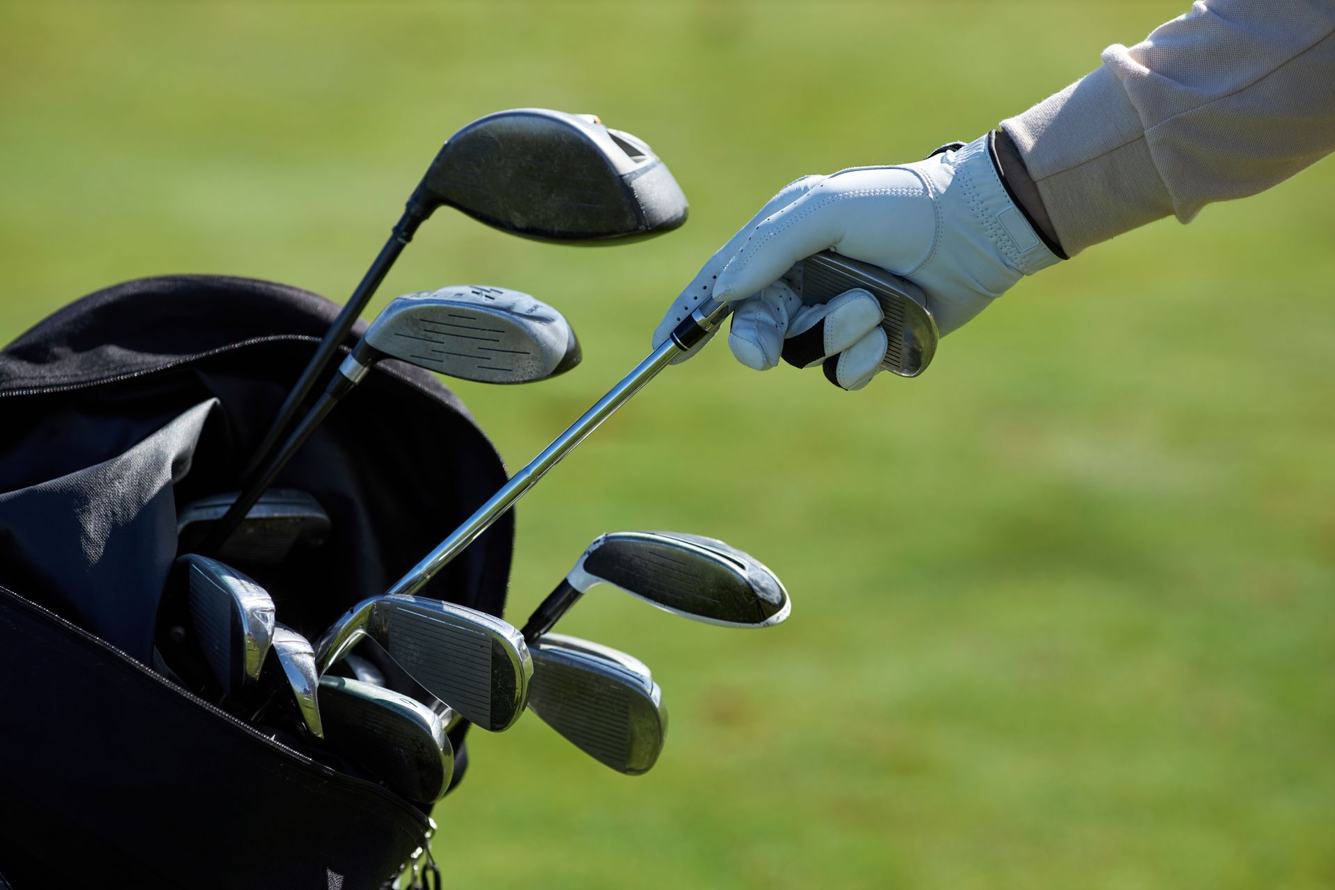 Hand in a golf glove selecting a golf club from a bag on a green.
