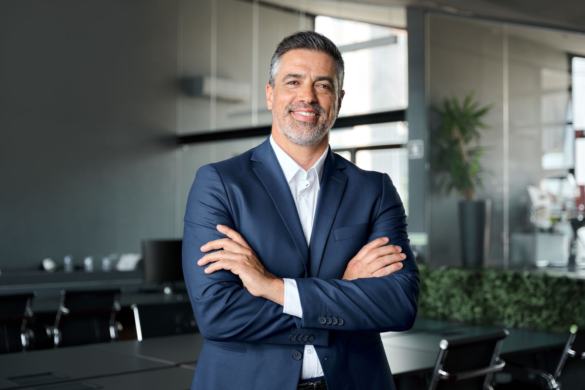 Man in a blue suit smiles with arms crossed in a conference room.
