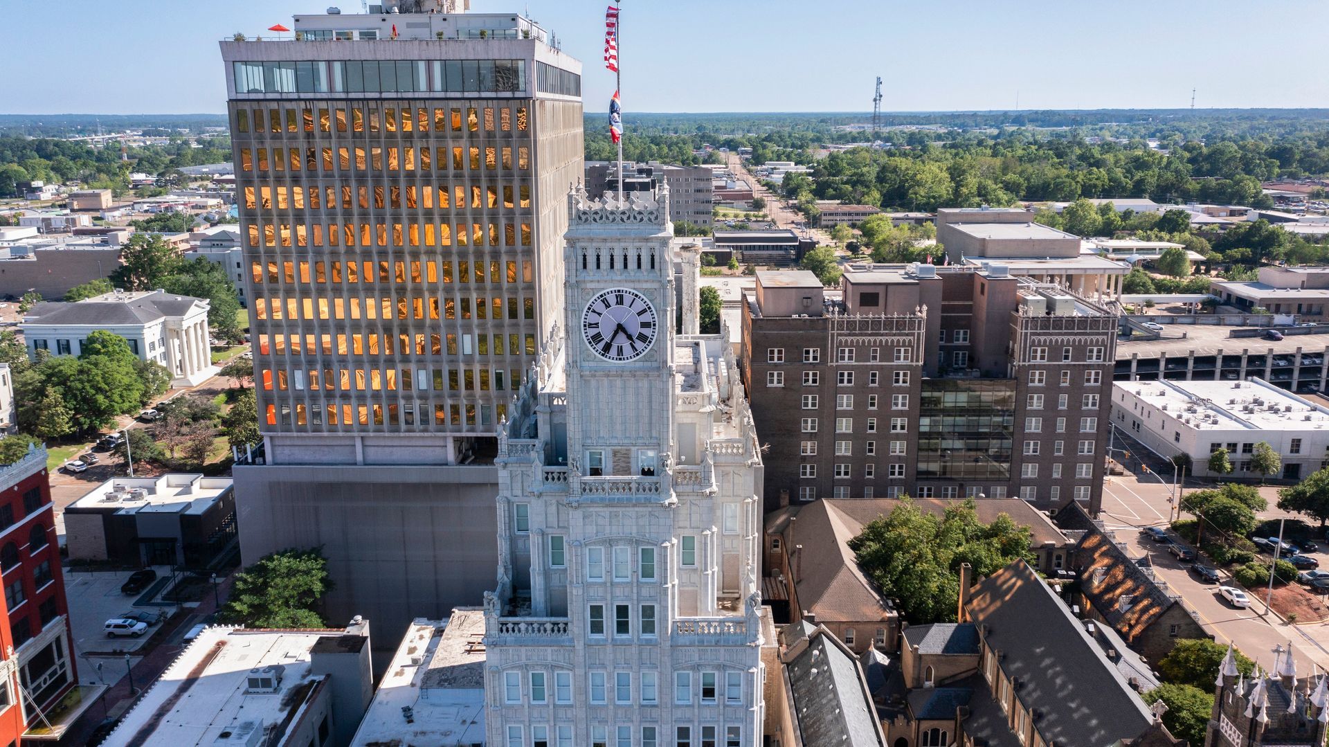Aerial view of downtown buildings with a clock tower in the foreground and a tall glass skyscraper.