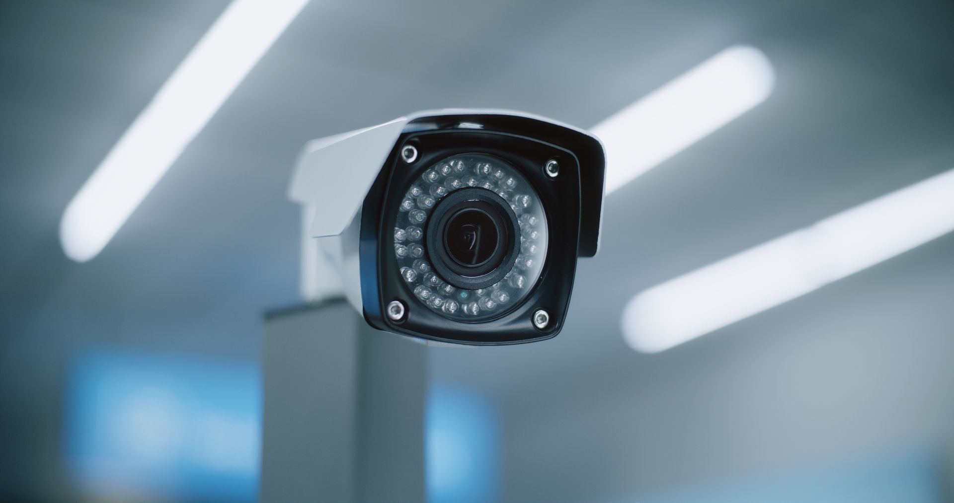Security camera mounted on a pole, indoor setting with bright lights.