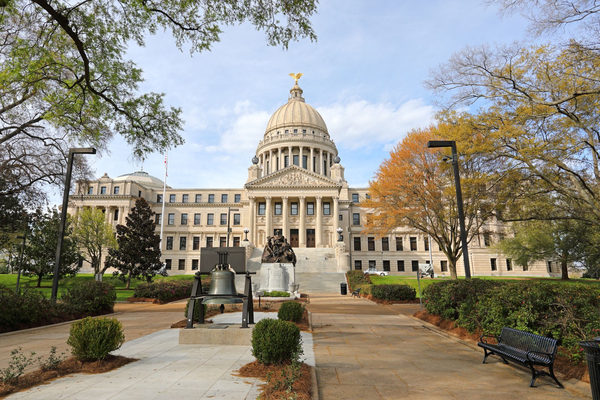 Mississippi State Capitol building with green lawn, trees, and walking path.
