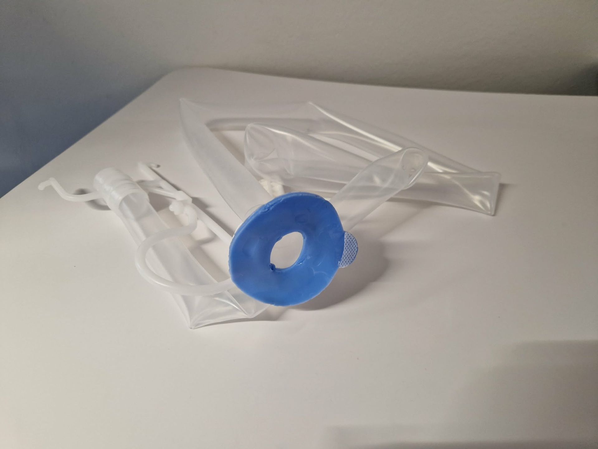Clear plastic medical supplies with a blue circular piece on a white table.