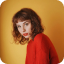A woman in a red sweater is standing in front of a yellow wall.
