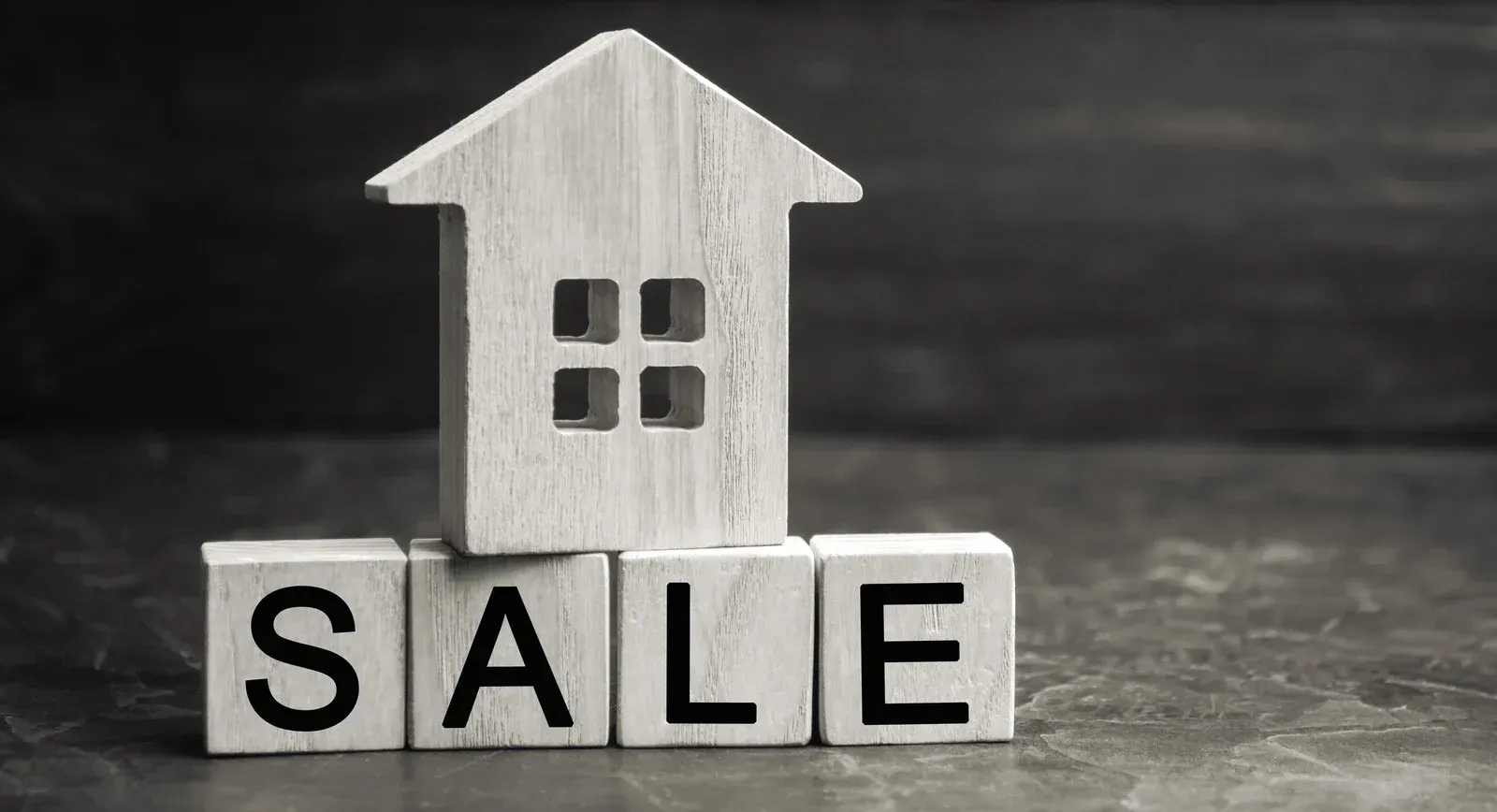A wooden house-shaped cutout sits atop four wooden blocks spelling out