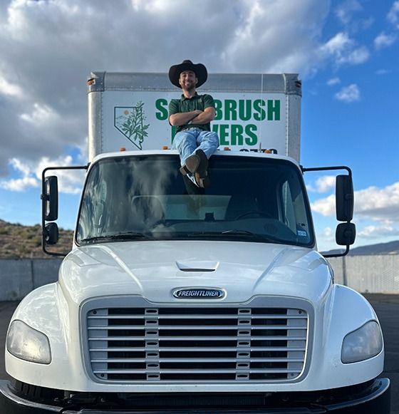 Man in cowboy hat sits on the cab of a white moving truck. Truck has Nevada license plate.