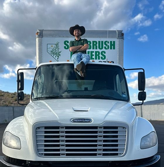 Man in cowboy hat sits on the cab of a white moving truck. Truck has Nevada license plate.