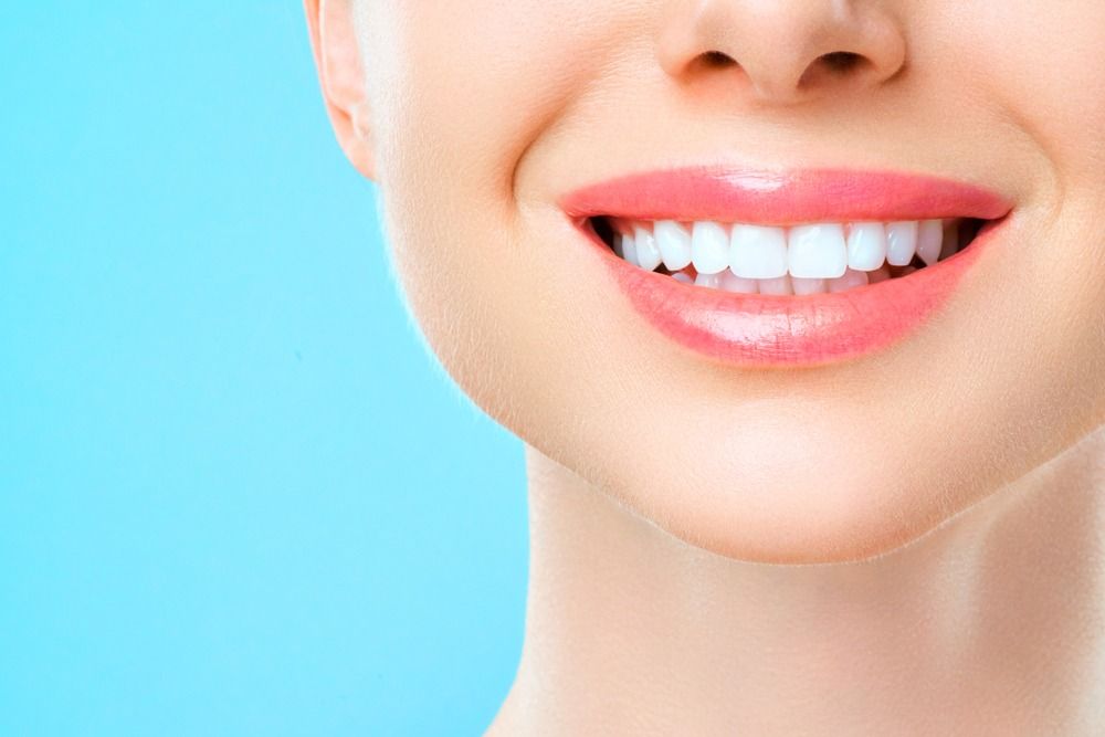 Close-up of a smiling mouth with white teeth against a bright blue background