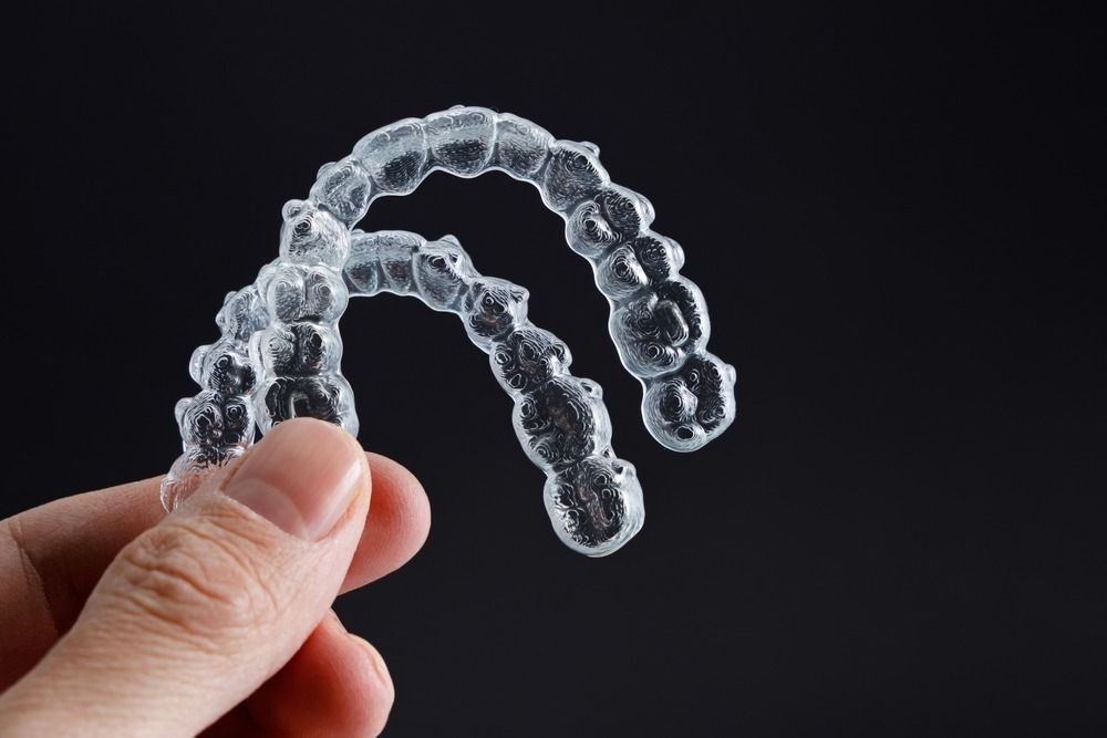 Hand holding clear plastic dental aligners against a black background