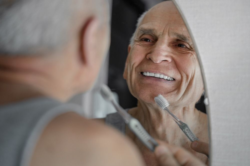 Smiling person brushing teeth while looking in a bathroom mirror