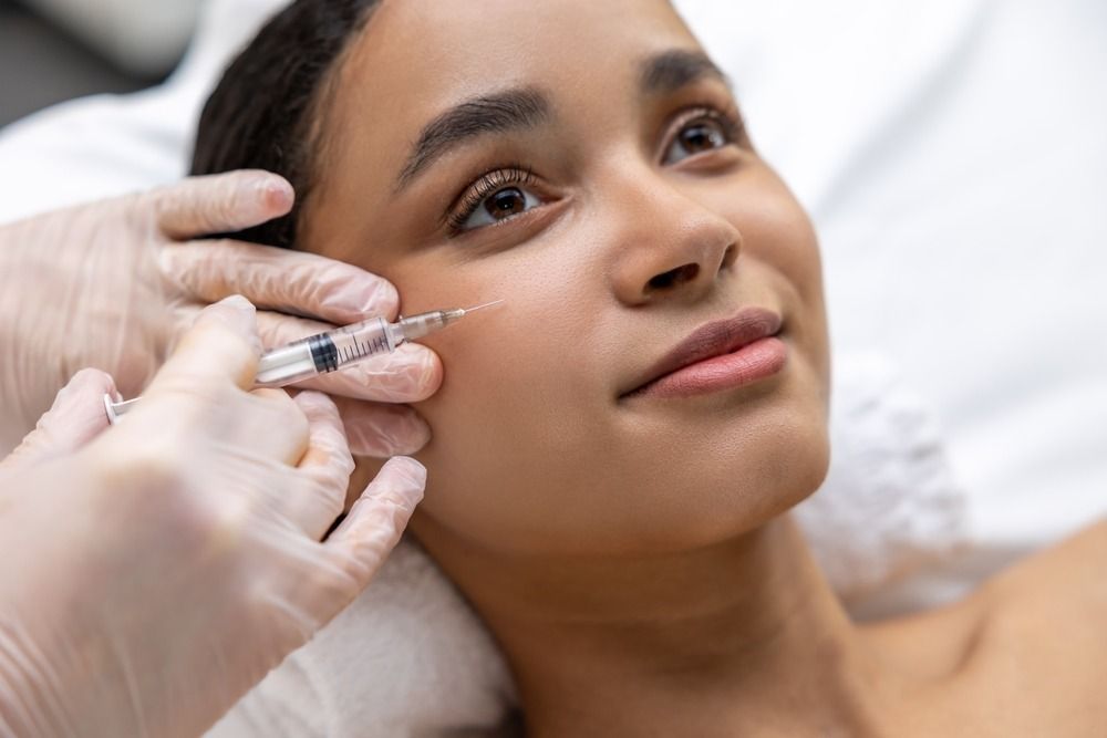 Cosmetic injection being administered to a smiling woman lying on a white treatment bed