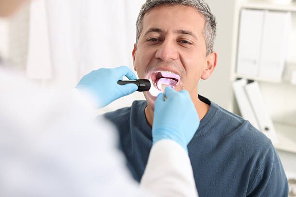 Dentist examining a patient’s open mouth with a dental mirror and gloved hands.