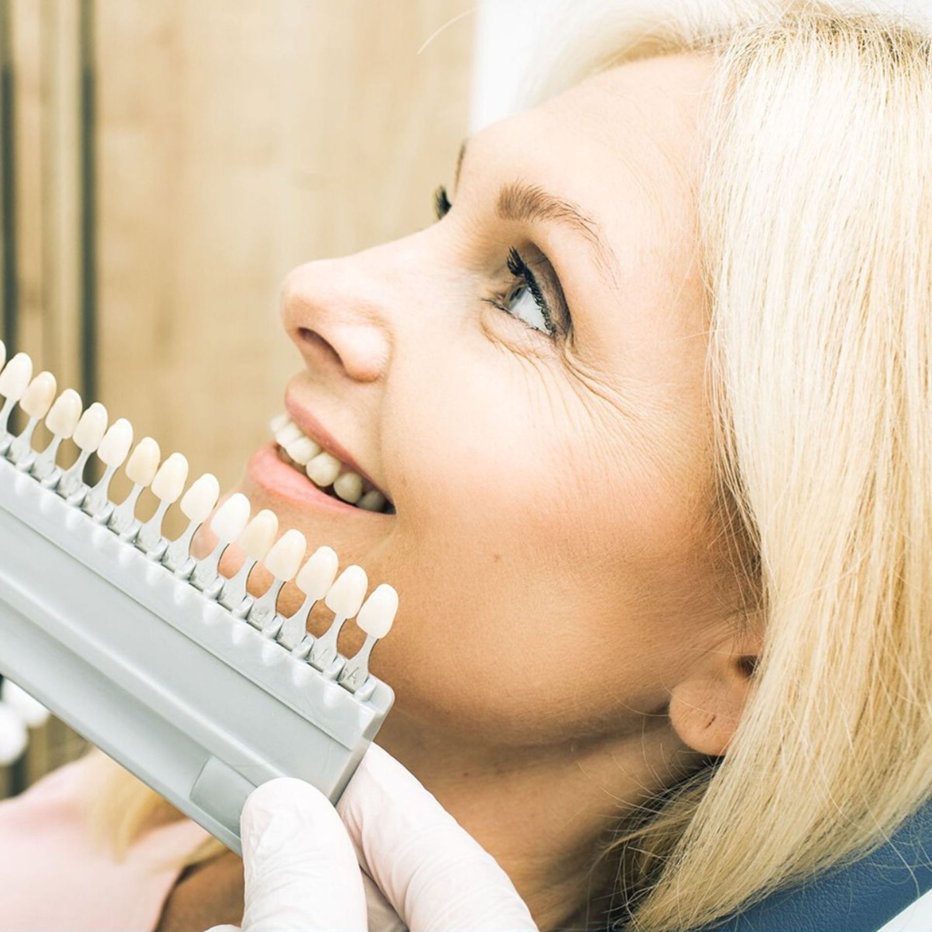 Woman smiling while comparing teeth shade samples in a dental office.