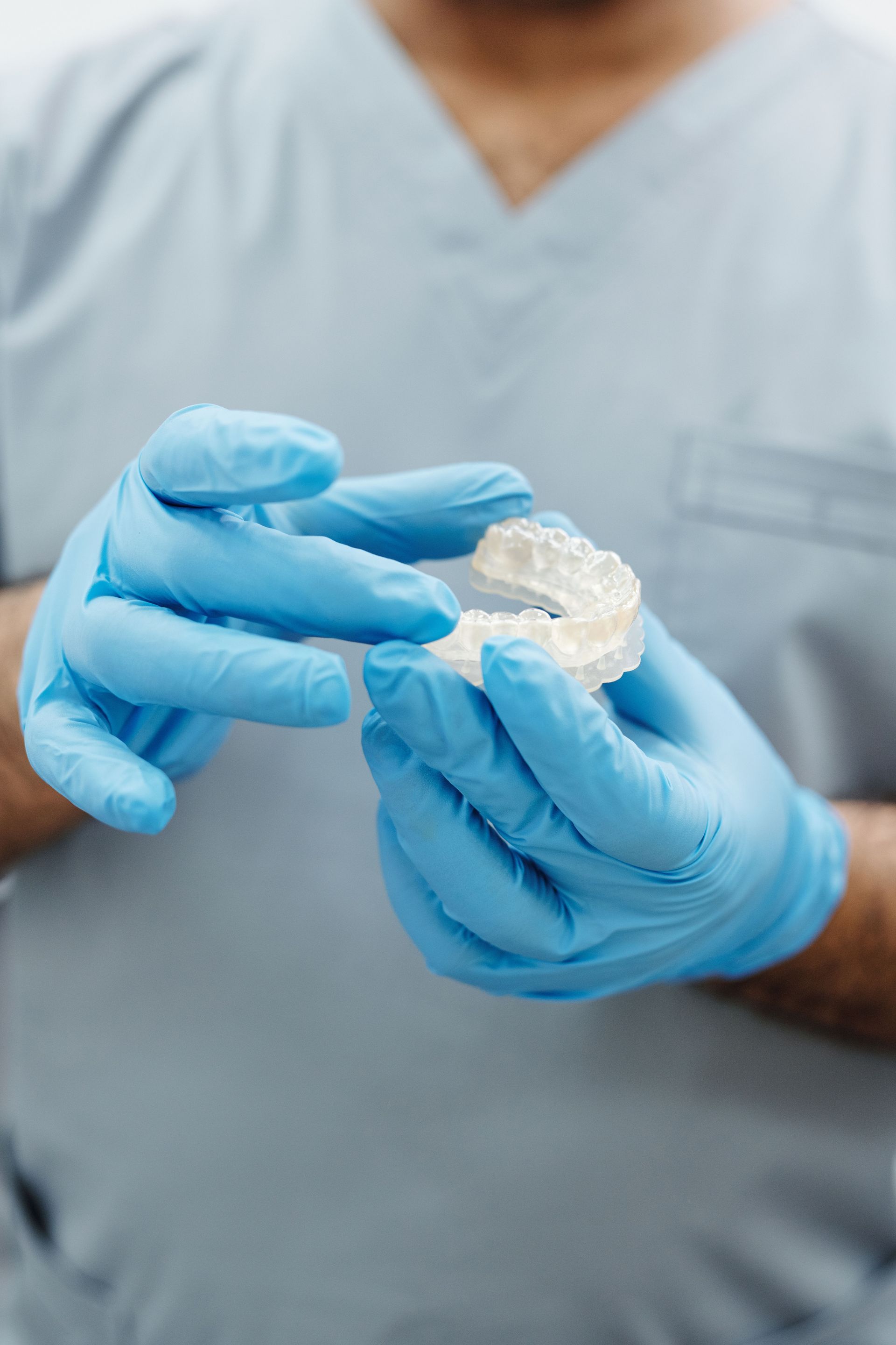 Blue-gloved hands handling a clear dental mold in a medical setting.