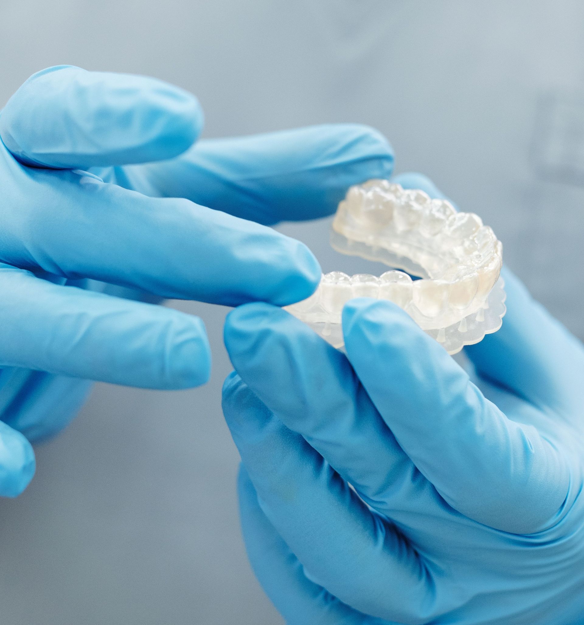 Blue-gloved hands holding a clear dental aligner.