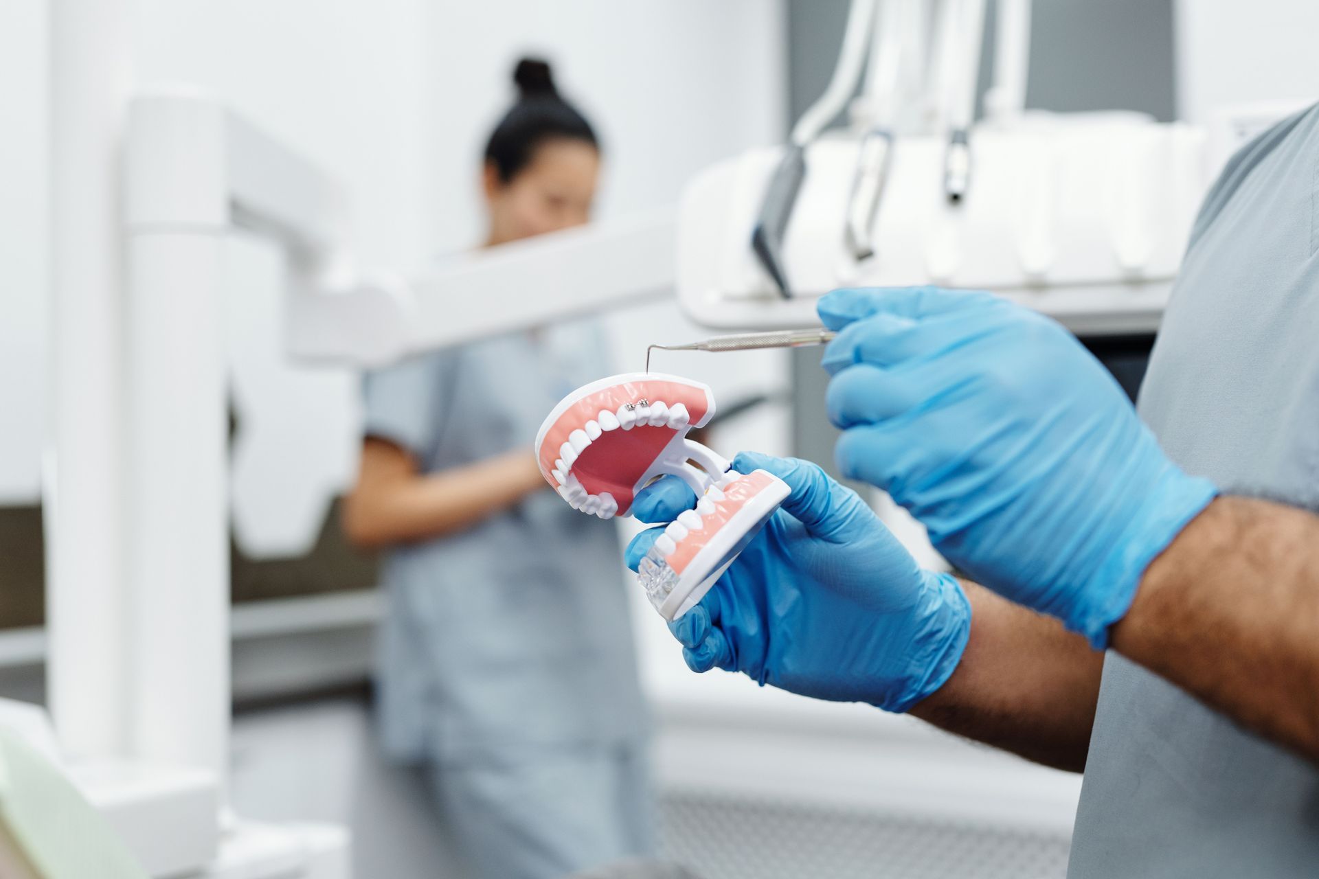 Dentist holding a dental model in blue gloves with a patient.