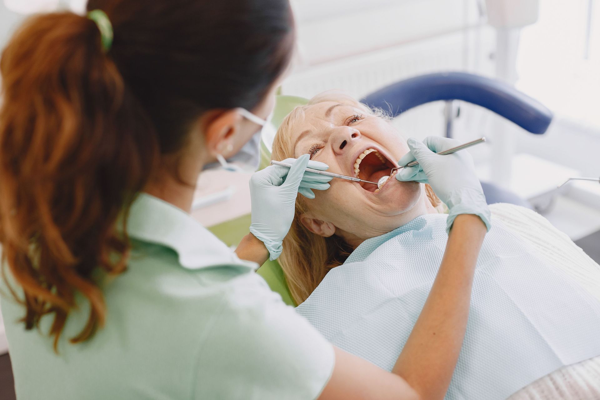 Dentist examining a patient in a dental chair, using tools during a checkup.