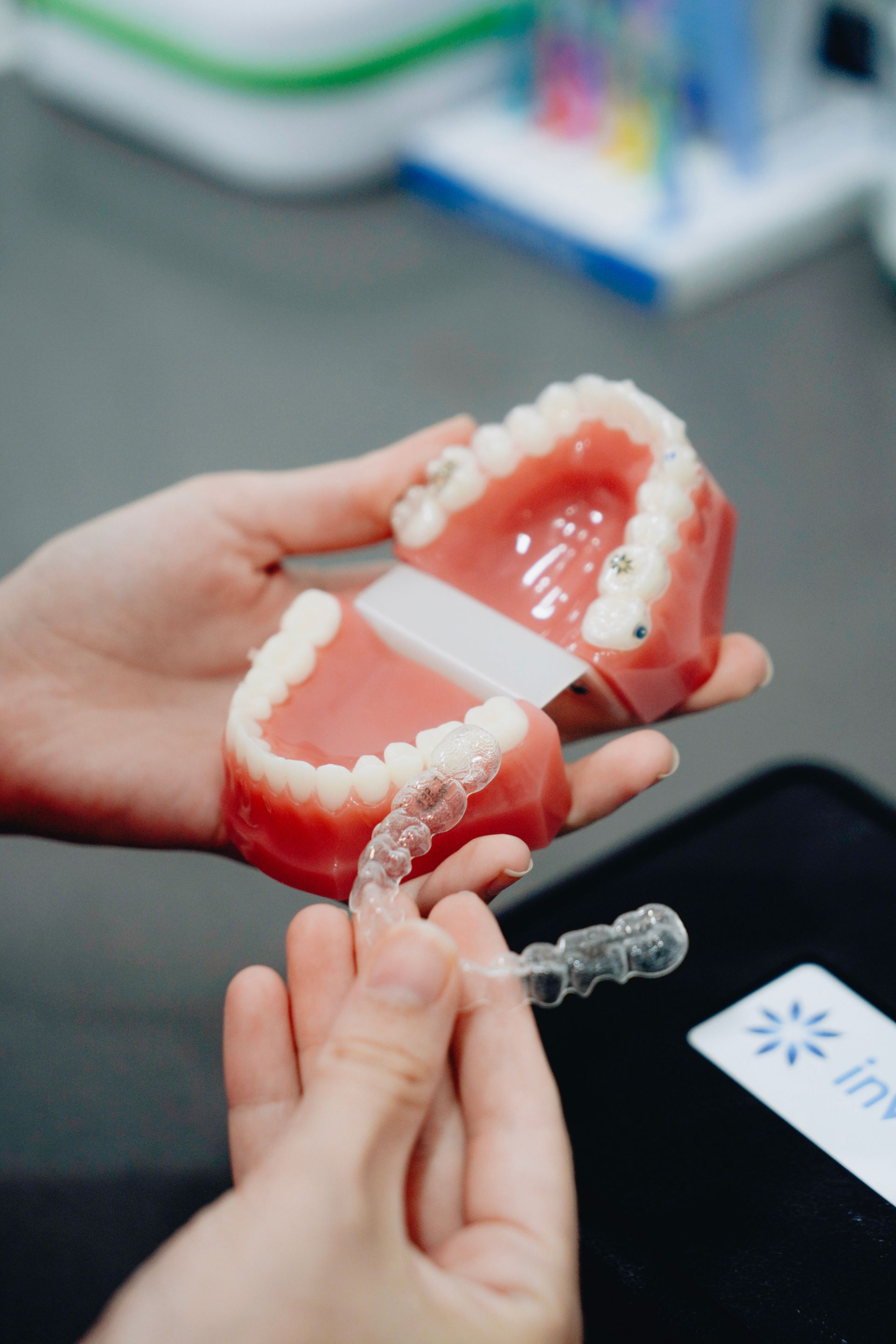 Hands holding a dental model and clear aligner in a clinic setting.
