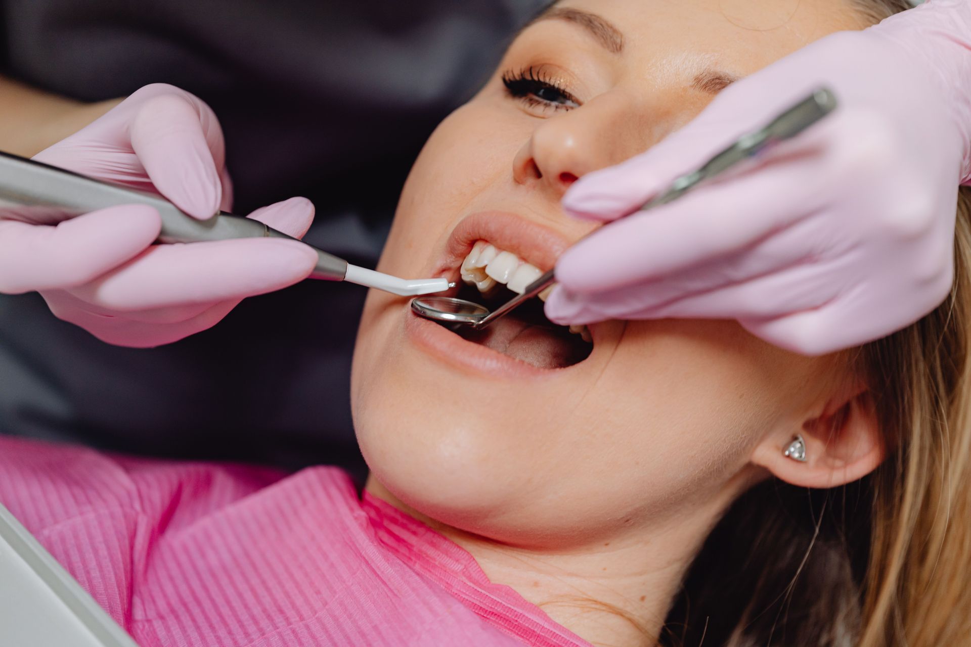 Dentist examining patient’s teeth with dental tools while the patient lies back in a chair.
