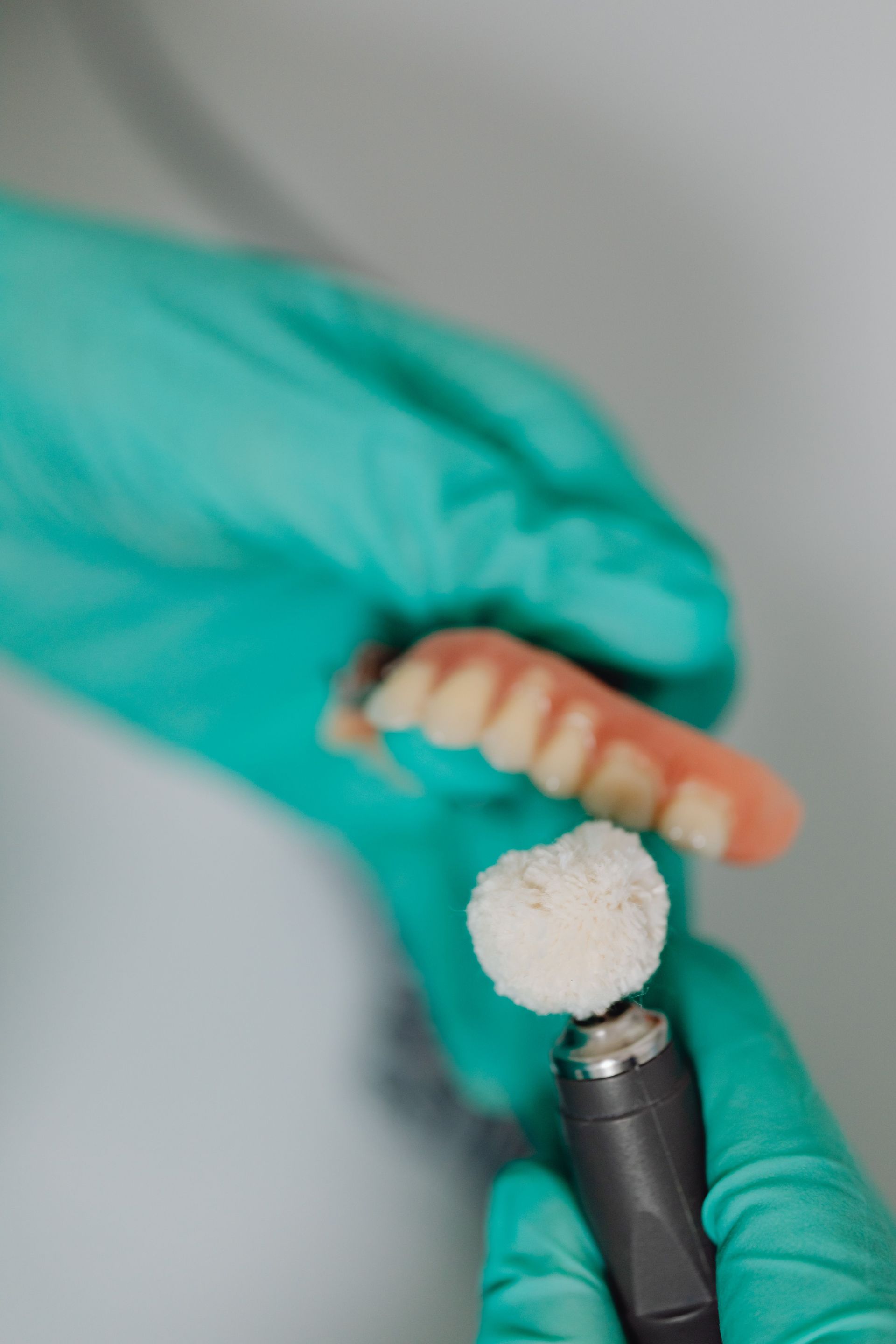 Gloved hands holding a dental mold and a rotary polishing tool with white compound.