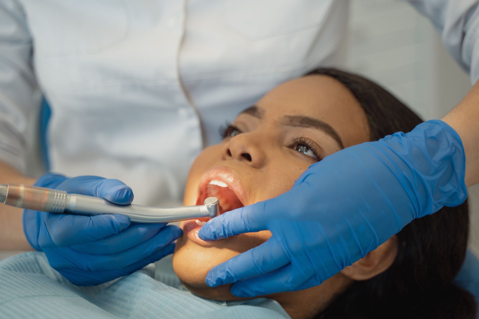 Dentist examining patient’s open mouth with dental tools and blue gloves.
