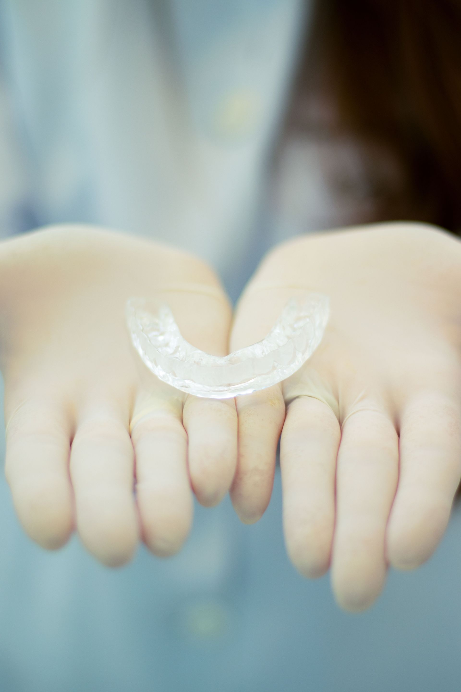 Hands holding a clear dental retainer against a soft blue background.