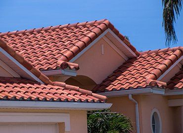 Red tile roof on a pale peach colored house against a bright blue sky.