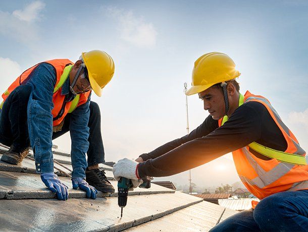 Two construction workers installing roof panels, wearing hard hats, safety vests, and gloves.