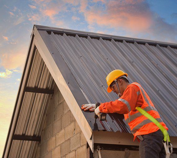 Roofer in safety gear installing metal panels on a roof against a cloudy sky.