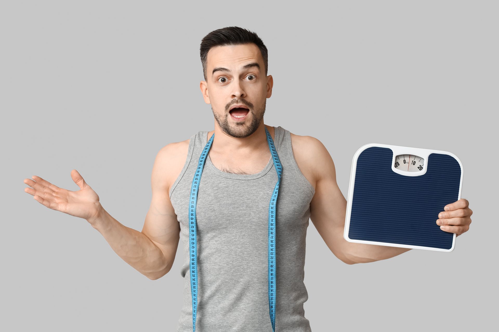 A man with a measuring tape around his neck is holding a scale.