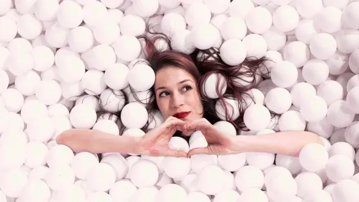 woman in a white ball pit making a love heart gesture