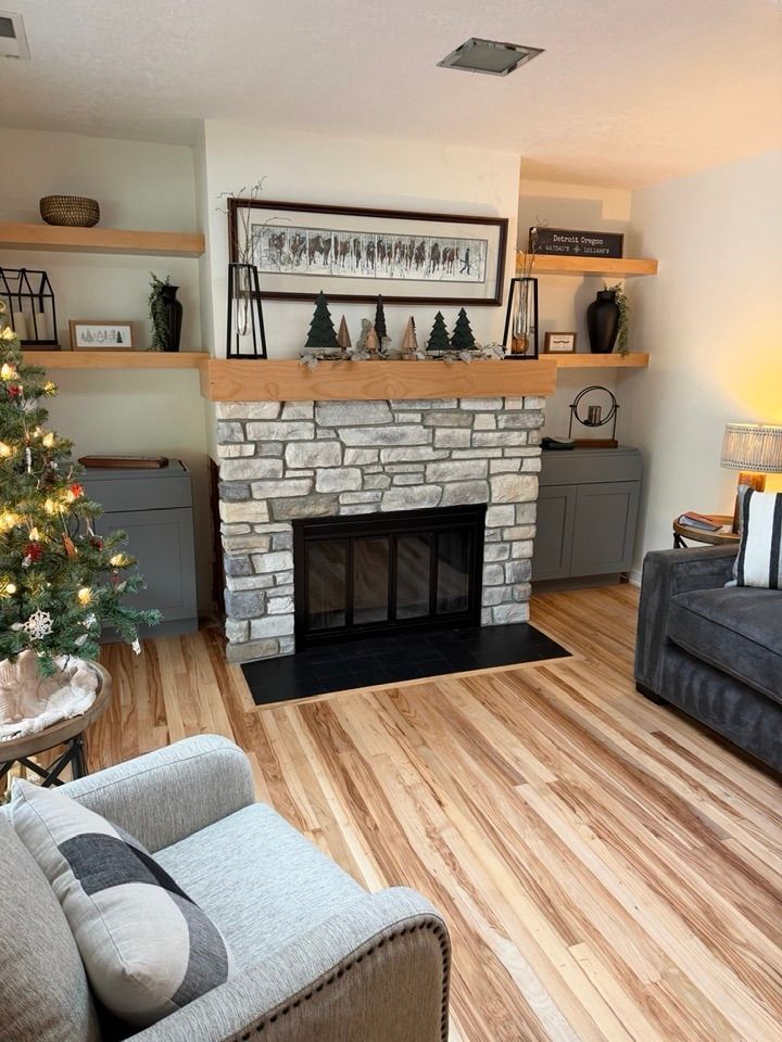Living room with a stone fireplace, wood mantel, built-in shelving, holiday decor, and gray furniture.